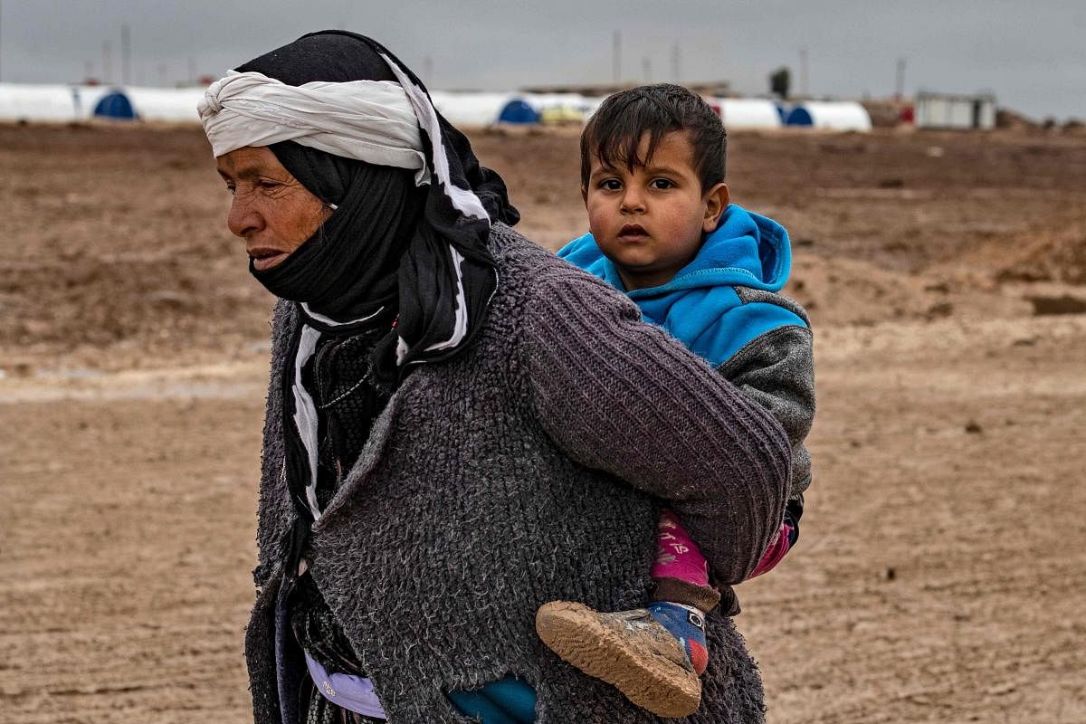 A Syrian woman walks by carrying a child on her back in the Washukanni Camp for the internally displaced, near the predominantly Kurdish city of Hasakeh in northeastern Syria. (AFP Photo)