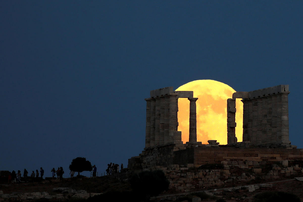 People watch a full moon rising behind the Temple of Poseidon before a lunar eclipse in Cape Sounion, near Athens, Greece, July 27, 2018. REUTERS/Alkis Konstantinidis 