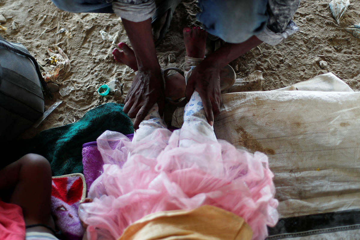 Satyendra Kumar, a migrant worker, massages the feet of her daughter after walking for three days, as they wait to cross the border to their home state of Uttar Pradesh, during an extended nationwide lockdown to slow the spread of the coronavirus disease (COVID-19), in New Delhi, India, May 17, 2020. Credit: Reuters Photo