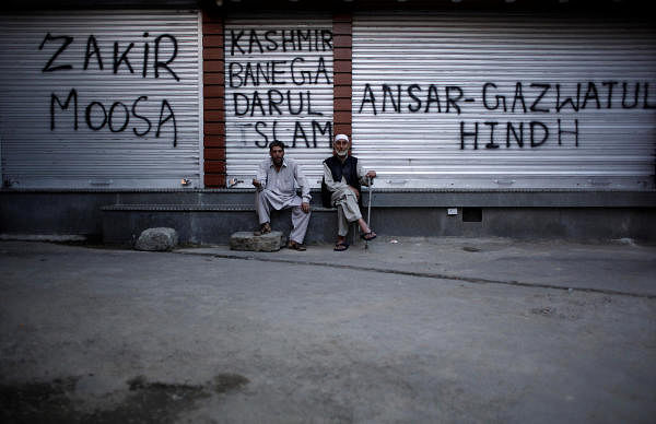 Kashmiri men sit in front of the closed shops painted with graffiti during restrictions after scrapping of the special constitutional status for Kashmir by the Indian government, in Srinagar, August 20, 2019. (Photo by Reuters)
