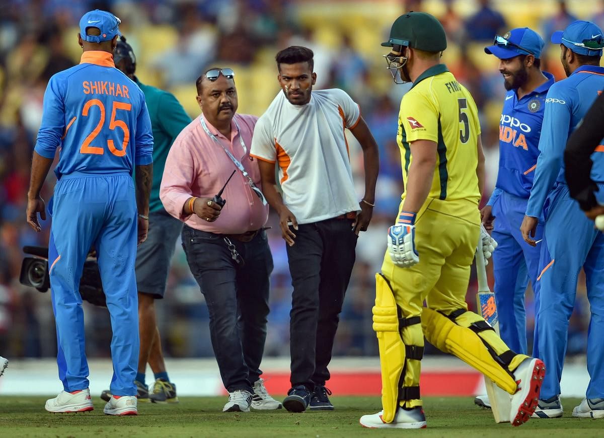 A security person tackles a pitch-invader who ran to the playing area to greet MS Dhoni during the 2nd ODI cricket match against Australia at Vidarbha Cricket Association Stadium in Nagpur. PTI