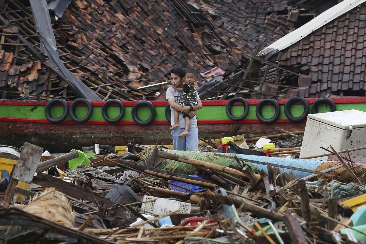 A man holds a child as he surveys the damage at a village struck by a tsunami in Sumur, Indonesia, Tuesday, Dec. 25, 2018. The waves struck without warning three days earlier. AP/PTI