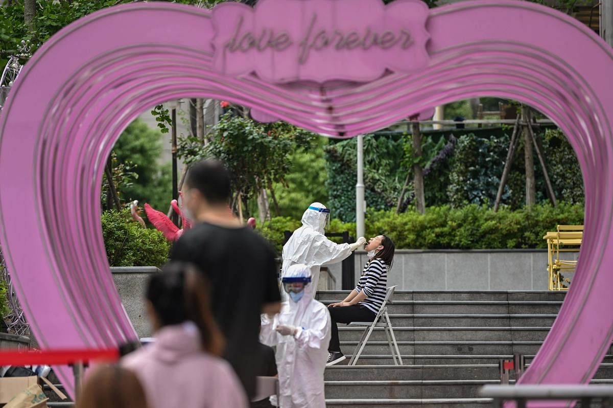 A medical worker takes a swab sample from a woman to be tested for the COVID-19 coronavirus while people wait in a line for testing next to a shopping mall in Wuhan, in China’s central Hubei province on May 16, 2020. Credit: AFP Photo