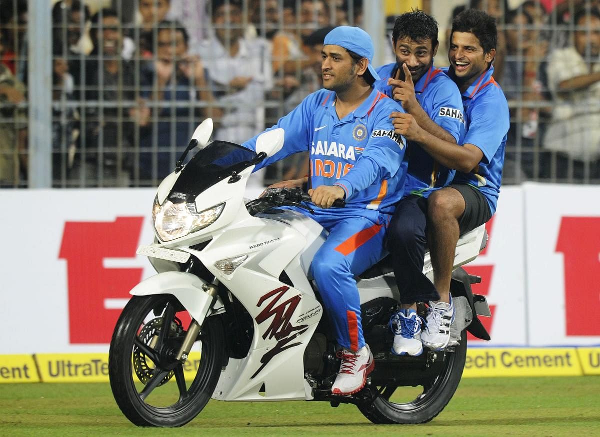 Former Indian cricket captain Mahendra Singh Dhoni rides a bike as teammate Praveen Kumar and Suresh Raina ride with him after winning the final ODI match between India and England at Eden Gardens Cricket Stadium in Kolkata. Credit: AFP Photo