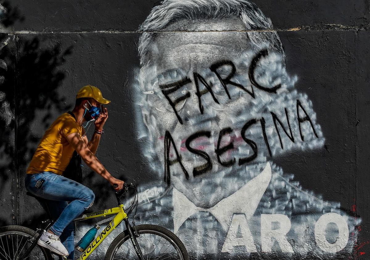 A man rides a bike by a mural against former Colombian President (2002-2010) Alvaro Uribe, which was covered and now shows a graffiti against the FARC (Revolutionary Armed Forces of Colombia). It was the most powerful guerrilla group on the American continent and is now the reformed FARC political party, in Bogota on September 5, 2020. Colombian ex-president Alvaro Uribe, who is being held under house arrest accused of fraud and witness tampering, resigned as senator last month. Credit: AFP Photo