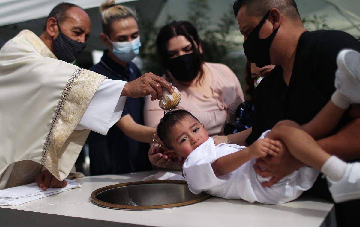 The Rev Arturo Corral baptizes a child outdoors at the historic Our Lady Queen of Angels (La Placita) Church amid the Covid-19 pandemic in Los Angeles, California. Congregants from separate families are seated in socially distanced chairs and required to wear face coverings to prevent the spread of the coronavirus. While the Covid-19 pandemic originally caused a backlog of around 600 baptisms at the church, La Placita is now able to conduct the ceremonies outdoors for the faithful in the church plaza. The church, dedicated in 1822 when California was a part of Mexico, primarily serves members of the Latino community and is the oldest Catholic church in Los Angeles. Credit: AFP Photo