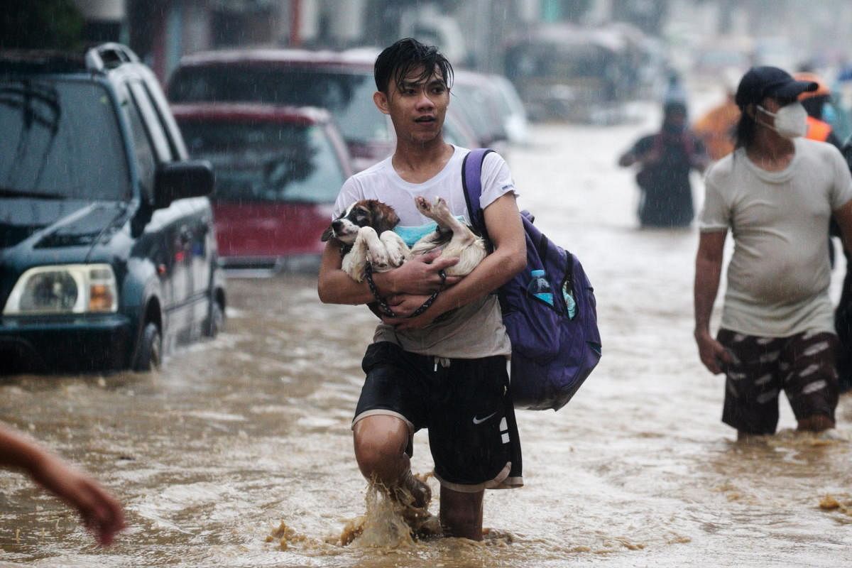 A man carries a dog as he evacuates from a flooded community following Typhoon Vamco, Philippines. Credit: Reuters Photo