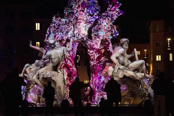 People view the Fountain of the Four Rivers (Fontana dei Quattro Fiumi) on piazza Navona in central Rome, illuminated with a new light mapping as part of the city's Christmas season, during the Covid-19 pandemic caused by the novel coronavirus. Credit: AFP