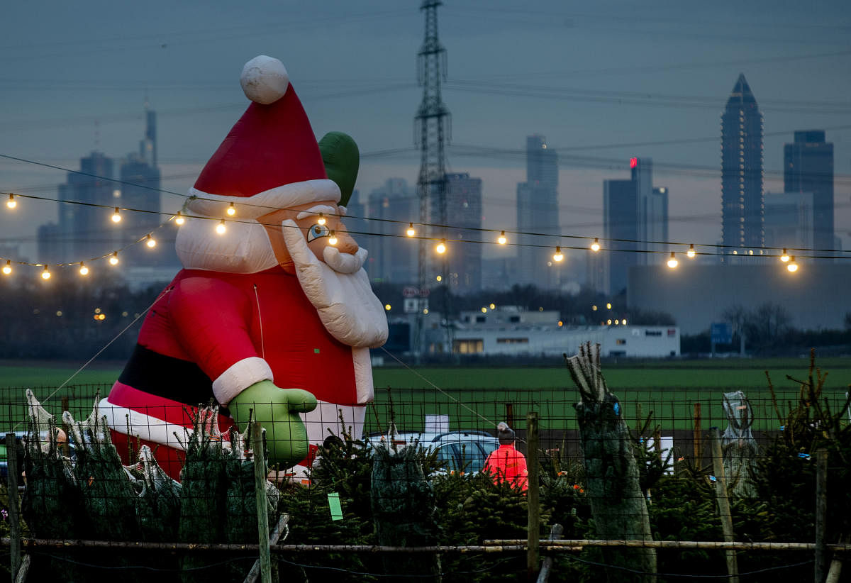 An inflatable Santa Claus decorates a Christmas tree sale in Frankfurt, Germany. Credit: AP/PTI