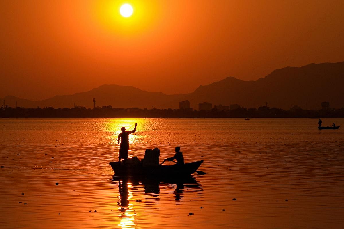 Fishermen silhouetted against the setting sun in the Anasagar Lake, in Ajmer. Credit: PTI