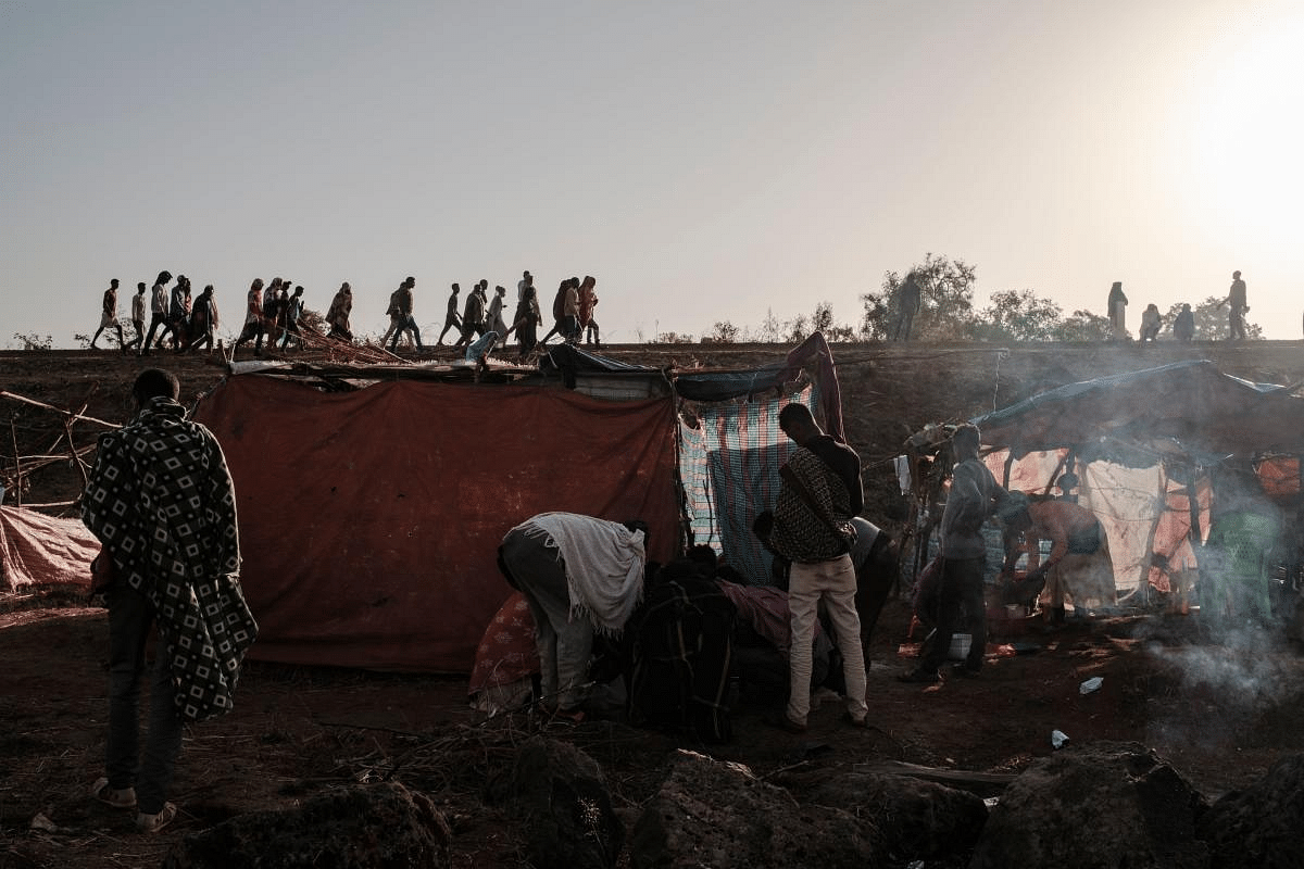 Internally Displaced People (IDP), fleeing from violence in the Metekel zone in Western Ethiopia, walk on a route as others stand next to huts in a camp in Chagni, Ethiopia. Credit: AFP Photo