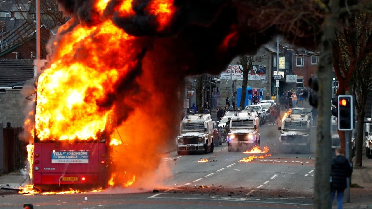 Police vehicles are seen behind a hijacked bus burns on the Shankill Road as protests continue in Belfast, Northern Ireland. Credit: Reuters Photo