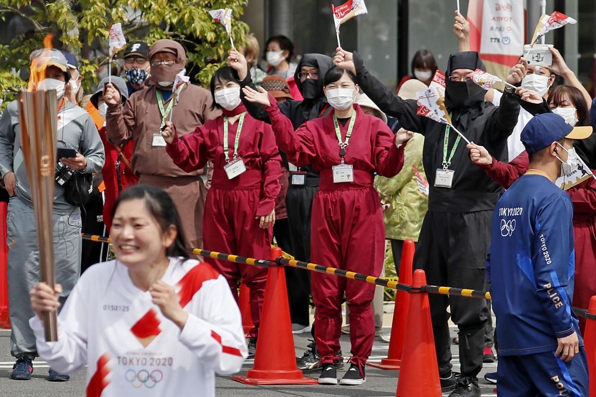  Spectators wearing face masks and ninja outfits, cheer a torchbearer carrying the Olympic torch in Iga, Mie prefecture, central Japan. Credit: AP Photo