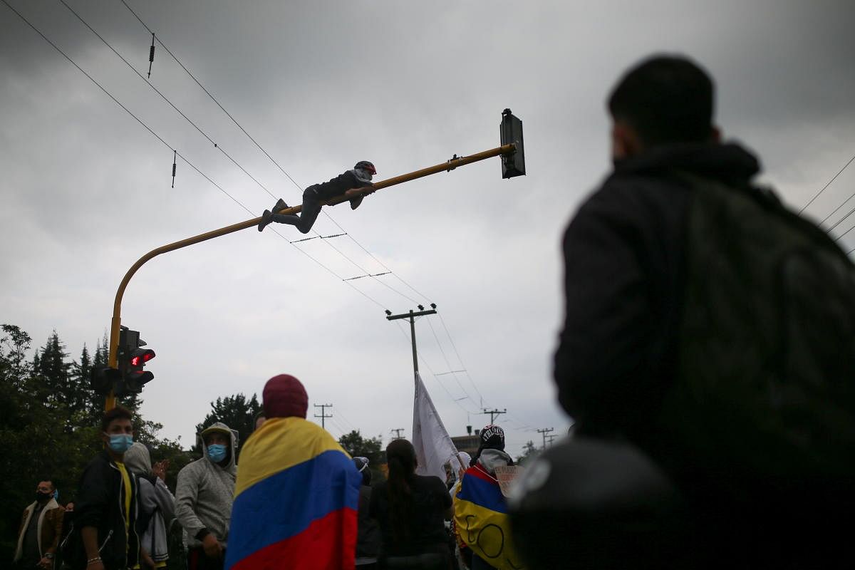 A demonstrator climbs traffic lights during a protest demanding government action to tackle poverty, police violence and inequalities in healthcare and education systems, in Bogota, Colombia. Credit: Reuters Photo