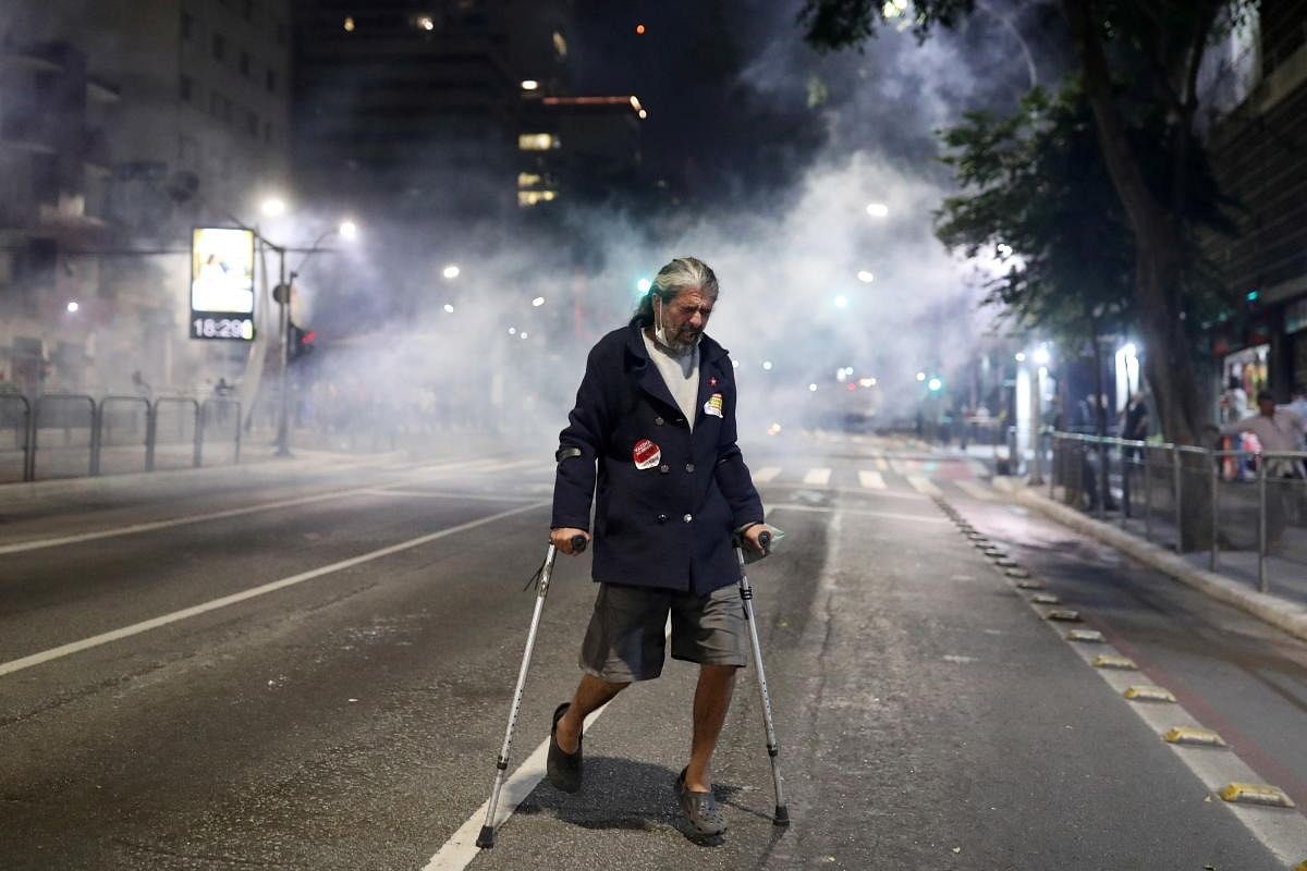 A man on crutches moves away from tear gas thrown by police during a protest to demand the impeachment of Brazil's President Jair Bolsonaro and against his handling of the coronavirus disease in Brazil. Credit: Reuters Photo