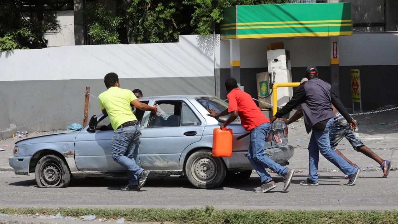 Men push a car from a gas station ransacked by people angry after the station refused to distribute fuel amid a nationwide shortage, in Port-au-Prince. Credit: Reuters photo