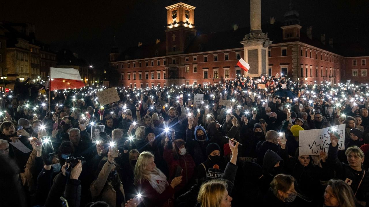 Protesters hold up lights, a Polish flag, posters reading "not even one more" and also photographs of Iza as they take part in a demonstration on November 6, 2021 in Warsaw, Poland, to mark the first anniversary of a Constitutional Court ruling that imposed a near-total ban on abortion, and also to commemorate the death of pregnant Polish woman Iza. Credit: Reuters Photo
