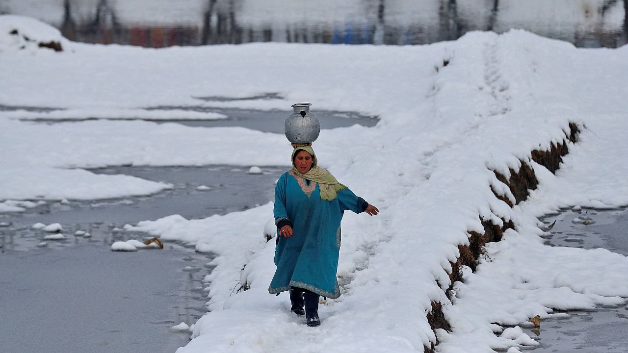 A woman carrying a water pitcher walks through a snow-covered field on the outskirts of Srinagar. Credit: Reuters Photo