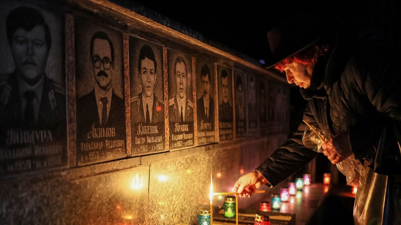 A woman lights a candle at a memorial dedicated to firefighters and workers who died after the Chornobyl nuclear disaster, during a night service in Slavutych. Credit: Reuters File Photo