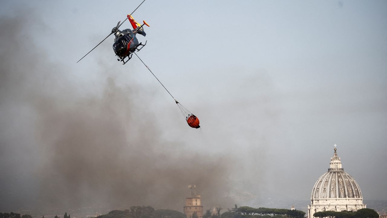 A firefighting helicopter drops water to extinguish a forest fire, with St. Peter's Basilica in the background, in north Rome, Italy, July 4, 2022. Credit: Reuters Photo