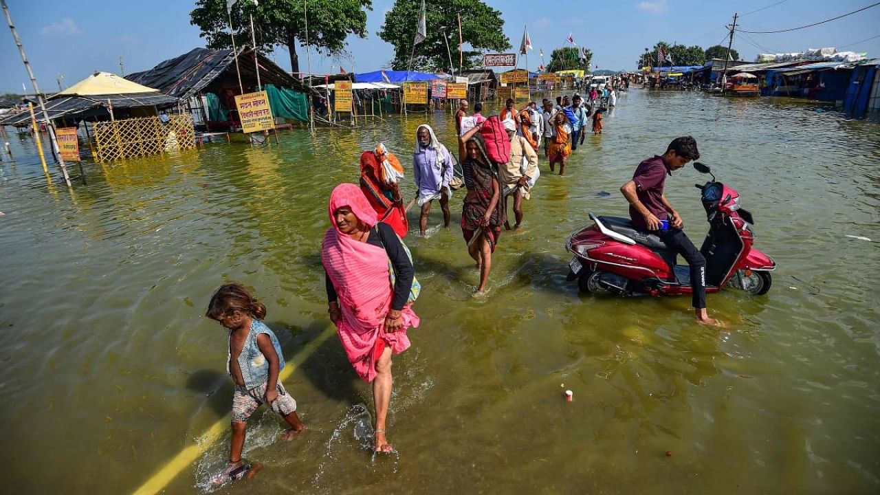 People wade through a flooded path near Sangam, the confluence of the Ganges, Yamuna and mythical Saraswati rivers after the water level of river Ganges and river Yamuna rose, in Allahabad on October 14, 2022. Credit: AFP Photo
