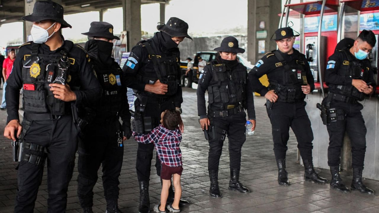 A migrant child from Venezuela hugs the legs of a police officer at a public bus station in Guatemala City, Guatemala, October 15, 2022. Credit: Reuters Photo