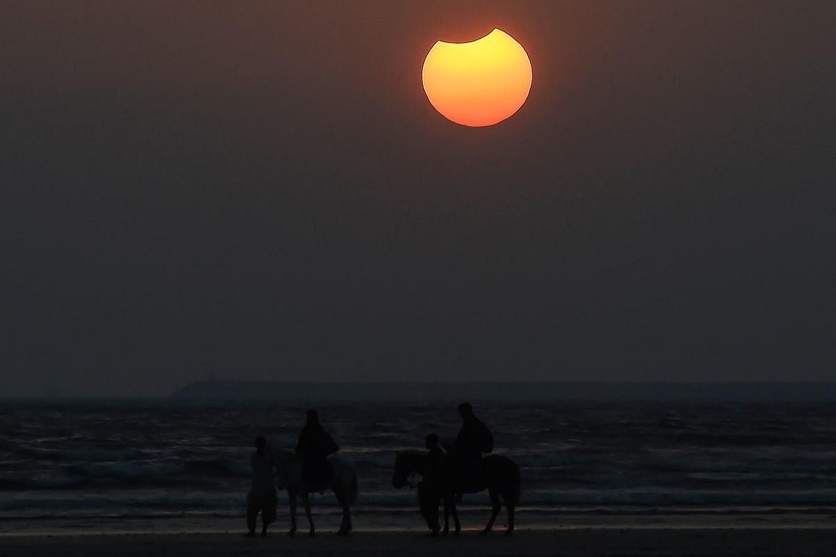 Men lead horses carrying turists along a beach as the moon partially obscures the sun during a partial solar eclipse visible from Karachi. Credit: AFP Photo