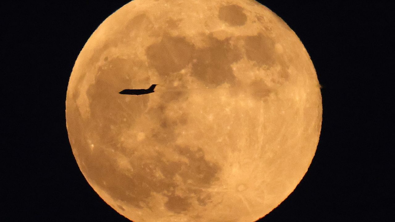 A commercial airline aircraft flies before the rising full moon above Kuwait City on November 8, 2022. Credit: AFP Photo