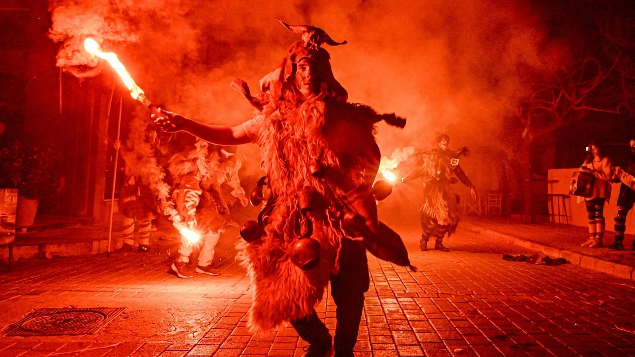 A costumed reveller lights a flare during a procession marking a traditional carnival celebration in the city of Amfissa, central Greece, on February 25, 2023. Credit: AFP Photo