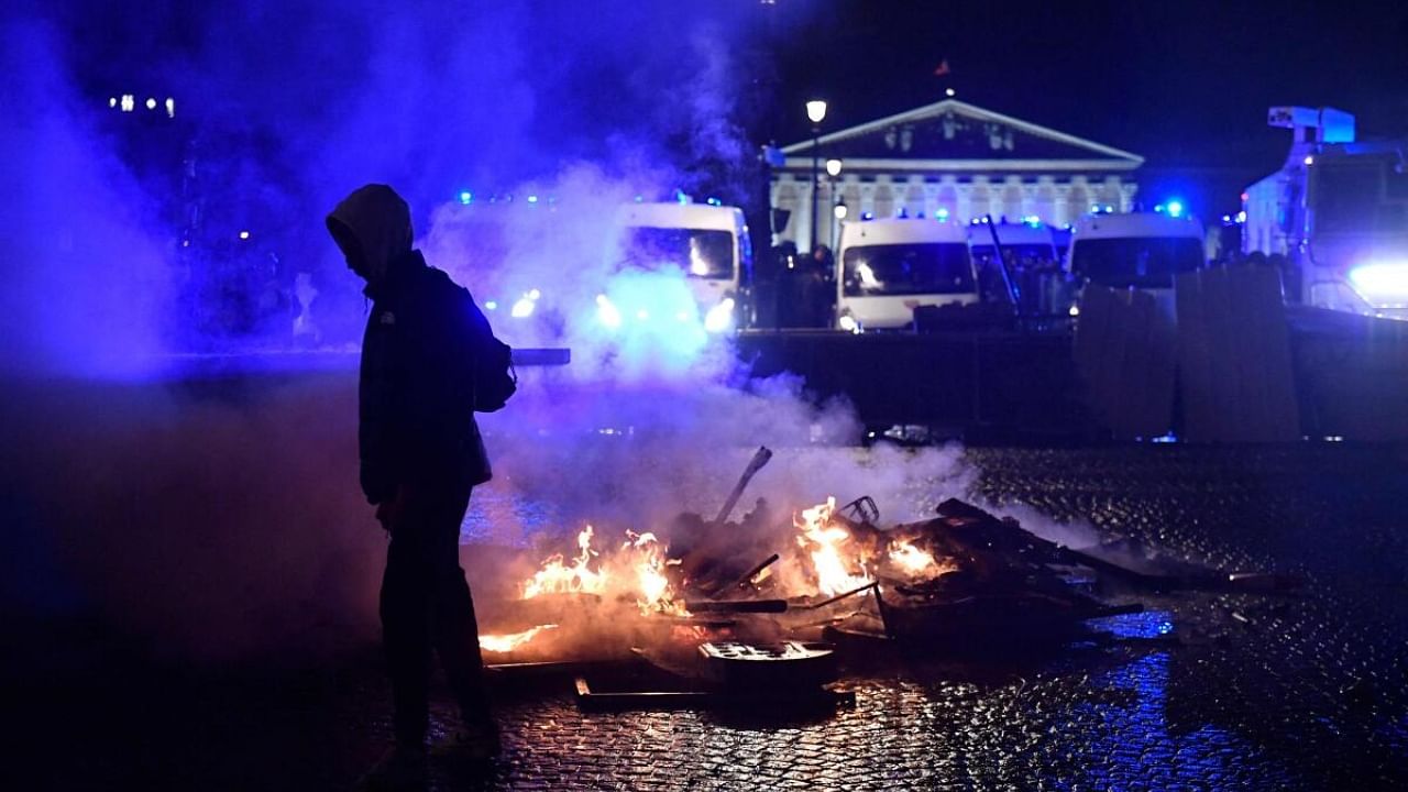 A protester walks past burning barriers during a demonstration on Place de la Concorde in Paris on March 17, 2023. Credit: AFP Photo