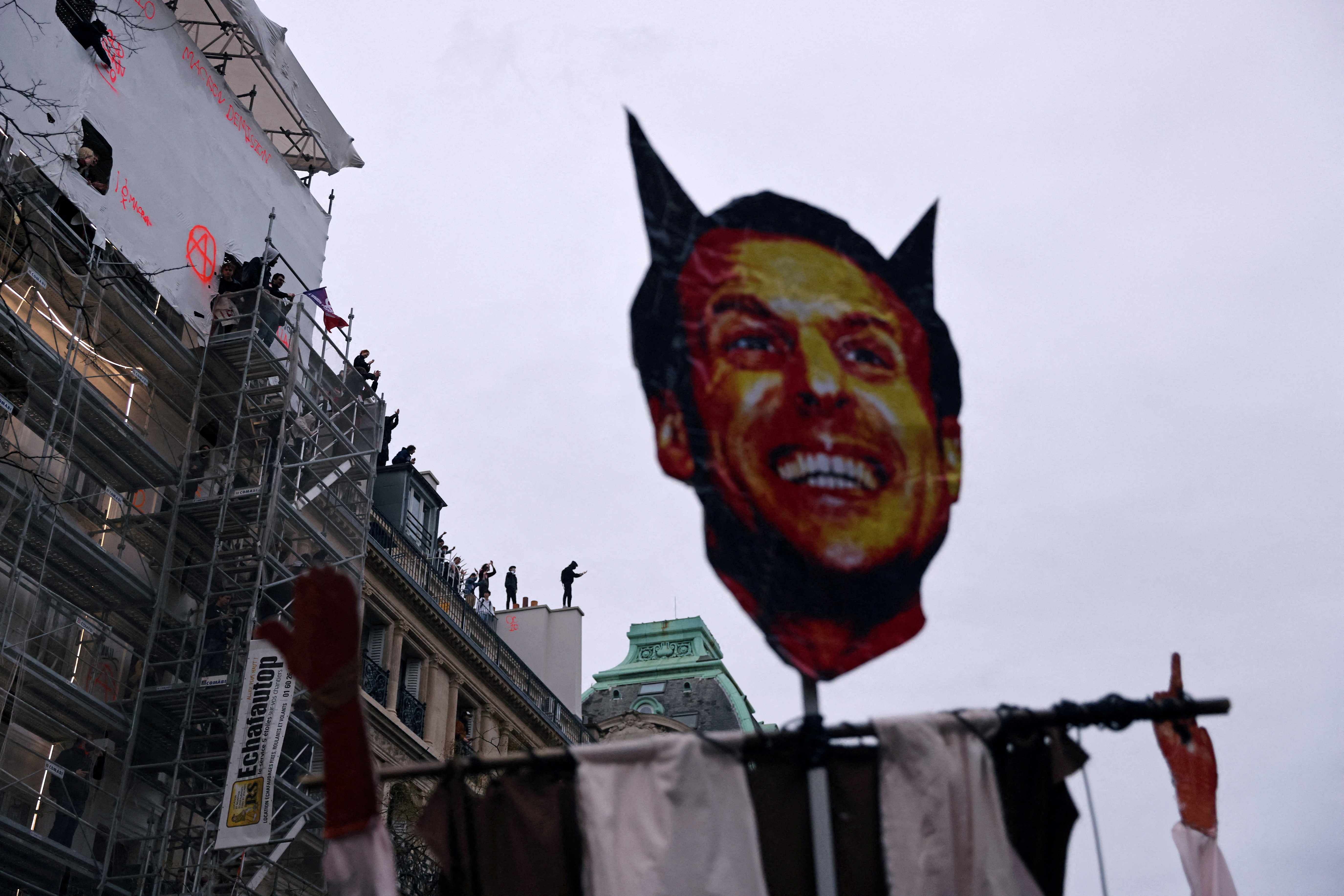 A placard with a portrait of French President Emmanuel Macron as the devil is seen as protesters stand on the top of a Parisian building during a demonstration as part of the ninth day of nationwide strikes and protests against French government's pension reform, in Paris, France, March 23, 2023. Credit: Reuters Photo
