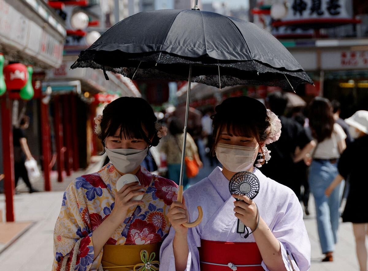 Women wearing summer kimonos use portable fans and an umbrella as they walk on the street. Credit: Reuters Photo