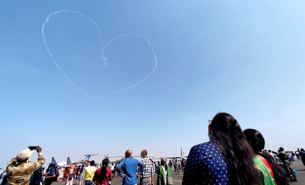 Visitors look skyward to a stunning piece of formation by IAF's Suryakiran aerobatic team that leaves behinda heart-shaped smoke trail on the concluding day of Aero India on Friday.